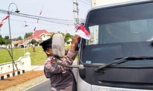 Personel Polsek Buay Madang Timur (BMT) memasangkan bendera merah putih pada tiap kendaraan yang melintas.