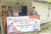 Kapolsek Buay Madang Timur, IPTU Swisspo, (kedua dari kiri), menyerahkan secara simbolis bantuan sembako kepada salah satu warga Desa Kumpul Rejo dalam rangka memperingati HUT Bhayangkara ke-80. 