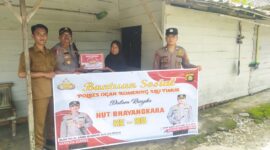 Kapolsek Buay Madang Timur, IPTU Swisspo, (kedua dari kiri), menyerahkan secara simbolis bantuan sembako kepada salah satu warga Desa Kumpul Rejo dalam rangka memperingati HUT Bhayangkara ke-80. 