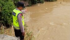 Anggota Piket Sabhara Polsek Buay Madang Timur, Aipda Sahrul Munir, memantau pergerakan arus dan debit air di aliran Sungai Macak, Desa Sukoharjo, Kecamatan Buay Madang Timur. 