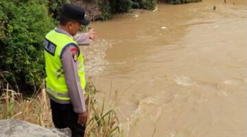 Anggota Piket Sabhara Polsek Buay Madang Timur, Aipda Sahrul Munir, memantau pergerakan arus dan debit air di aliran Sungai Macak, Desa Sukoharjo, Kecamatan Buay Madang Timur. 