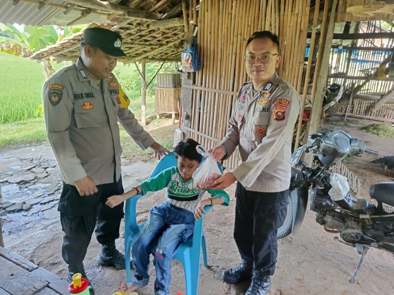 Bhabinkamtibmas Polsek Buay Madang Timur Bripka Nur Holik (kiri) bersama Brigadir Tedy Heryadi (kanan) menyerahkan paket daging kurban dari Kapolres OKU Timur kepada salah satu anak penyandang disabilitas di Desa Pengandonan, Kecamatan Buay Madang Timur, Kabupaten OKU Timur, Sumatera Selatan. 