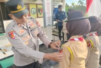 Kapolsek Buay Madang Timur, Iptu Swisspo, menyematkan tanda anggota kepada perwakilan Pramuka dalam Upacara Pelantikan Anggota Saka Bhayangkara Angkatan X di Mako Polsek Buay Madang Timur, Kabupaten OKU Timur. 