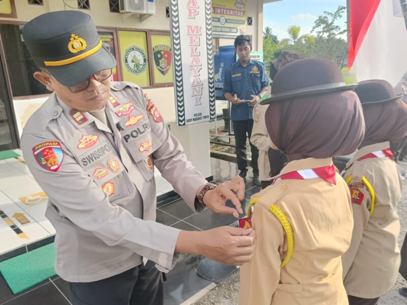 Kapolsek Buay Madang Timur, Iptu Swisspo, menyematkan tanda anggota kepada perwakilan Pramuka dalam Upacara Pelantikan Anggota Saka Bhayangkara Angkatan X di Mako Polsek Buay Madang Timur, Kabupaten OKU Timur. 