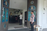 Personel Polsek Buay Madang Timur berjaga di depan pintu masuk Gereja Trinitas Bangun Sari BK 3, Kecamatan Buay Madang Timur, Kabupaten OKU Timur. 