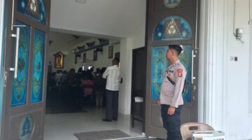 Personel Polsek Buay Madang Timur berjaga di depan pintu masuk Gereja Trinitas Bangun Sari BK 3, Kecamatan Buay Madang Timur, Kabupaten OKU Timur. 