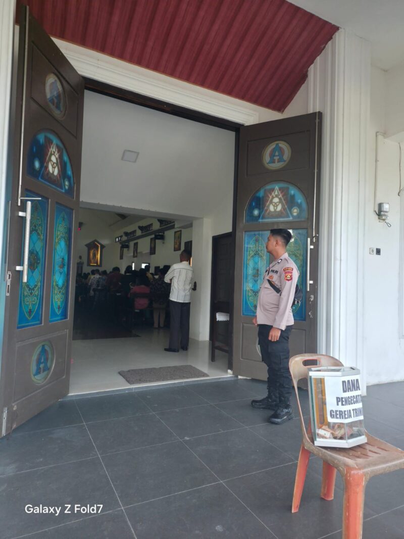 Personel Polsek Buay Madang Timur berjaga di depan pintu masuk Gereja Trinitas Bangun Sari BK 3, Kecamatan Buay Madang Timur, Kabupaten OKU Timur. 
