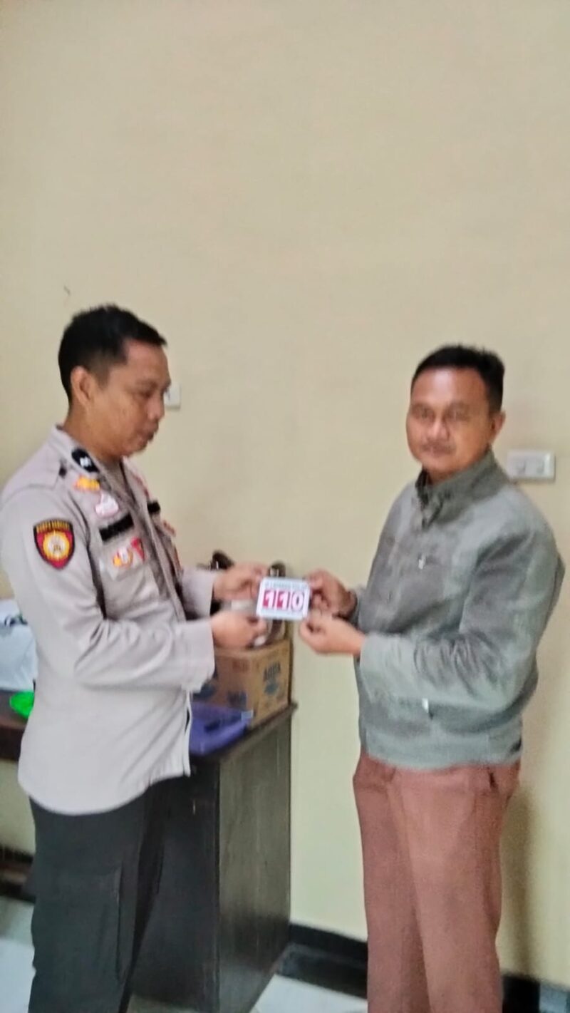 Kasium Polsek Buay Madang Timur AIPDA Robbiansyah (kiri) memberikan stiker informasi Layanan Kepolisian 110 kepada seorang warga di Mako Polsek Buay Madang Timur, Kabupaten OKU Timur. 