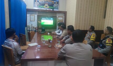 Sejumlah personel Polsek Buay Madang Timur bersama warga menyaksikan siaran langsung pertandingan Prancis vs Senegal dalam acara nonton bareng Pesta Bola Dunia 2026 di Mako Polsek Buay Madang Timur, Kabupaten OKU Timur, Sumatra Selatan.
