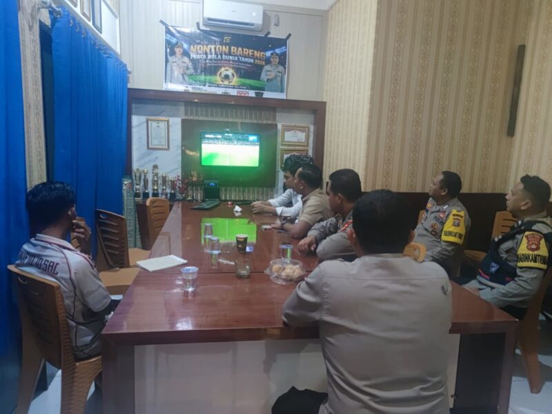 Sejumlah personel Polsek Buay Madang Timur bersama warga menyaksikan siaran langsung pertandingan Prancis vs Senegal dalam acara nonton bareng Pesta Bola Dunia 2026 di Mako Polsek Buay Madang Timur, Kabupaten OKU Timur, Sumatra Selatan. 