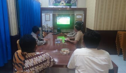 Kapolsek Buay Madang Timur Iptu Swisspo, bersama personel dan warga setempat menyaksikan pertandingan laga Pesta Bola Dunia 2026 antara Amerika Serikat melawan Australia di Mako Polsek Buay Madang Timur, Kabupaten OKU Timur.