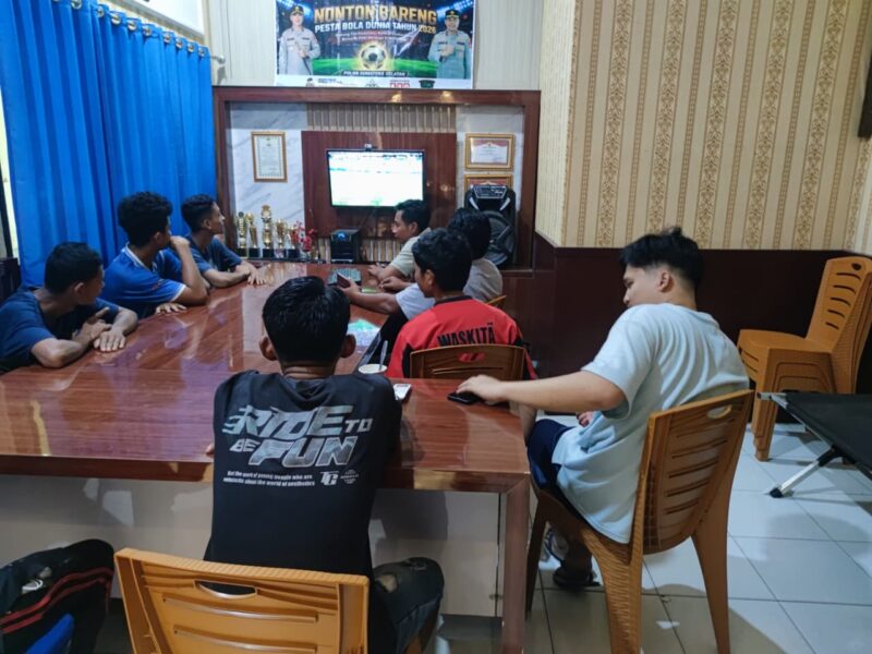 Jajaran anggota Polsek Buay Madang Timur bersama warga pencinta sepak bola saat menyaksikan pertandingan laga Pesta Bola Dunia 2026 antara Belgia vs Iran di Mako Polsek Buay Madang Timur, OKU Timur. 