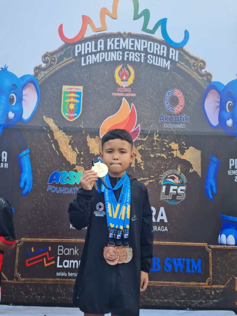 Atlet renang muda asal OKU Timur, Zakra Alkahfi Karim (Alfy), menunjukkan medali yang diraihnya pada Kejuaraan Renang Piala Kemenpora RI 2026 di Kolam Renang Pahoman, Bandar Lampung. 
