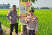 Kapolsek Buay Madang Timur Iptu Swisspo (kanan) bersama Bripka Didi Handoko memasang spanduk Layanan Kepolisian 110 dan imbauan larangan kebakaran hutan dan lahan (Karhutla) di Desa Wonodadi Asri, Kecamatan Buay Madang Timur, Kabupaten OKU Timur. 