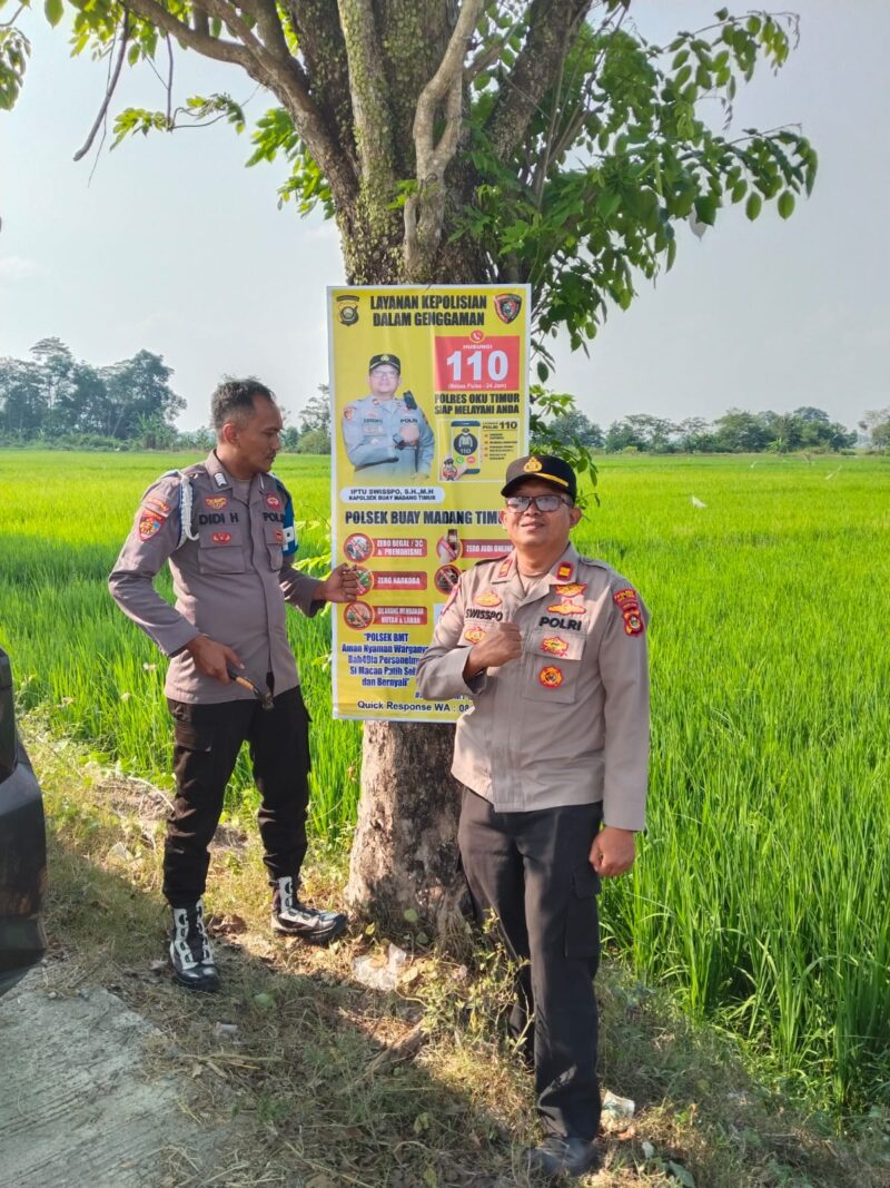 Kapolsek Buay Madang Timur Iptu Swisspo (kanan) bersama Bripka Didi Handoko memasang spanduk Layanan Kepolisian 110 dan imbauan larangan kebakaran hutan dan lahan (Karhutla) di Desa Wonodadi Asri, Kecamatan Buay Madang Timur, Kabupaten OKU Timur. 