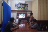 Anggota Polsek Buay Madang Timur bersama masyarakat pencinta sepak bola menyaksikan pertandingan Pesta Bola Dunia 2026 antara Inggris vs Argentina di Mako Polsek Buay Madang Timur, Kabupaten OKU Timur. 