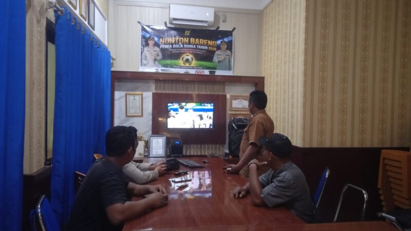 Anggota Polsek Buay Madang Timur bersama masyarakat pencinta sepak bola menyaksikan pertandingan Pesta Bola Dunia 2026 antara Inggris vs Argentina di Mako Polsek Buay Madang Timur, Kabupaten OKU Timur. 