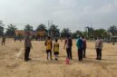 Personel Polsek BMT melakukan pengamanan melekat di tengah Lapangan Desa Karang Tengah saat berlangsungnya hari kedua Turnamen Sepak Bola Tingkat SD #BMT Cup 2026 di Kabupaten OKU Timur. 