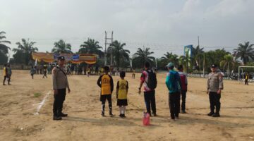 Personel Polsek BMT melakukan pengamanan melekat di tengah Lapangan Desa Karang Tengah saat berlangsungnya hari kedua Turnamen Sepak Bola Tingkat SD #BMT Cup 2026 di Kabupaten OKU Timur.