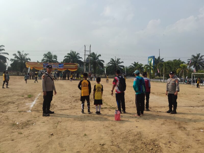 Personel Polsek BMT melakukan pengamanan melekat di tengah Lapangan Desa Karang Tengah saat berlangsungnya hari kedua Turnamen Sepak Bola Tingkat SD #BMT Cup 2026 di Kabupaten OKU Timur. 