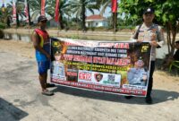 Personel piket Polsek Buay Madang Timur, Aipda Zulkifli dan Bripka Iswanto, membentangkan spanduk maklumat bersama warga saat melaksanakan Giat Sambang dan Sosialisasi Pencegahan Kebakaran Hutan dan Lahan (Karhutla) di wilayah Kecamatan Buay Madang Timur, Kabupaten OKU Timur.