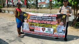Personel piket Polsek Buay Madang Timur, Aipda Zulkifli dan Bripka Iswanto, membentangkan spanduk maklumat bersama warga saat melaksanakan Giat Sambang dan Sosialisasi Pencegahan Kebakaran Hutan dan Lahan (Karhutla) di wilayah Kecamatan Buay Madang Timur, Kabupaten OKU Timur.