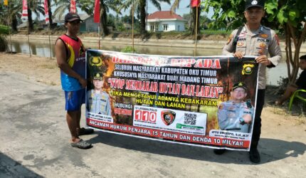 Personel piket Polsek Buay Madang Timur, Aipda Zulkifli dan Bripka Iswanto, membentangkan spanduk maklumat bersama warga saat melaksanakan Giat Sambang dan Sosialisasi Pencegahan Kebakaran Hutan dan Lahan (Karhutla) di wilayah Kecamatan Buay Madang Timur, Kabupaten OKU Timur.
