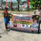 Personel piket Polsek Buay Madang Timur, Aipda Zulkifli dan Bripka Iswanto, membentangkan spanduk maklumat bersama warga saat melaksanakan Giat Sambang dan Sosialisasi Pencegahan Kebakaran Hutan dan Lahan (Karhutla) di wilayah Kecamatan Buay Madang Timur, Kabupaten OKU Timur.