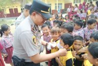 Kapolsek Buay Madang Timur (BMT) Iptu Swisspo, memasangkan masker secara langsung kepada salah seorang murid saat menggelar program Cooling System / Goes To School di SDN Rejodadi, Desa Rejodadi, Kecamatan Buay Madang Timur, OKU Timur.