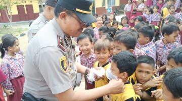 Kapolsek Buay Madang Timur (BMT) Iptu Swisspo, memasangkan masker secara langsung kepada salah seorang murid saat menggelar program Cooling System / Goes To School di SDN Rejodadi, Desa Rejodadi, Kecamatan Buay Madang Timur, OKU Timur.