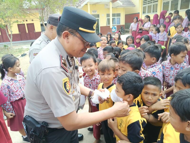 Kapolsek Buay Madang Timur (BMT) Iptu Swisspo, memasangkan masker secara langsung kepada salah seorang murid saat menggelar program Cooling System / Goes To School di SDN Rejodadi, Desa Rejodadi, Kecamatan Buay Madang Timur, OKU Timur.