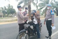 Kapolsek Buay Madang Timur, Iptu Swisspo, memakaikan masker gratis kepada seorang pengendara sepeda motor yang melintas di jalan raya Desa Karang Tengah, Kecamatan Buay Madang Timur, Kabupaten OKU Timur.