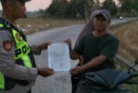 Personel Polsek Buay Madang Timur, Aipda Khoirul, menyerahkan lembaran Maklumat Kapolda Sumsel terkait larangan pembakaran hutan dan lahan kepada pengendara motor di Desa Sumber Mulyo, OKU Timur.
