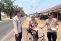 Bhabinkamtibmas Polsek Buay Madang Timur Aipda Wisnu Saputra didampingi Kanit Binmas Bripka Ari Wicaksono membagikan paket makanan kepada seorang warga pesepeda di Desa Karang Tengah, Kecamatan Buay Madang Timur, Kabupaten OKU Timur.