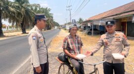 Bhabinkamtibmas Polsek Buay Madang Timur Aipda Wisnu Saputra didampingi Kanit Binmas Bripka Ari Wicaksono membagikan paket makanan kepada seorang warga pesepeda di Desa Karang Tengah, Kecamatan Buay Madang Timur, Kabupaten OKU Timur.