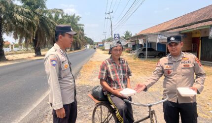 Bhabinkamtibmas Polsek Buay Madang Timur Aipda Wisnu Saputra didampingi Kanit Binmas Bripka Ari Wicaksono membagikan paket makanan kepada seorang warga pesepeda di Desa Karang Tengah, Kecamatan Buay Madang Timur, Kabupaten OKU Timur.