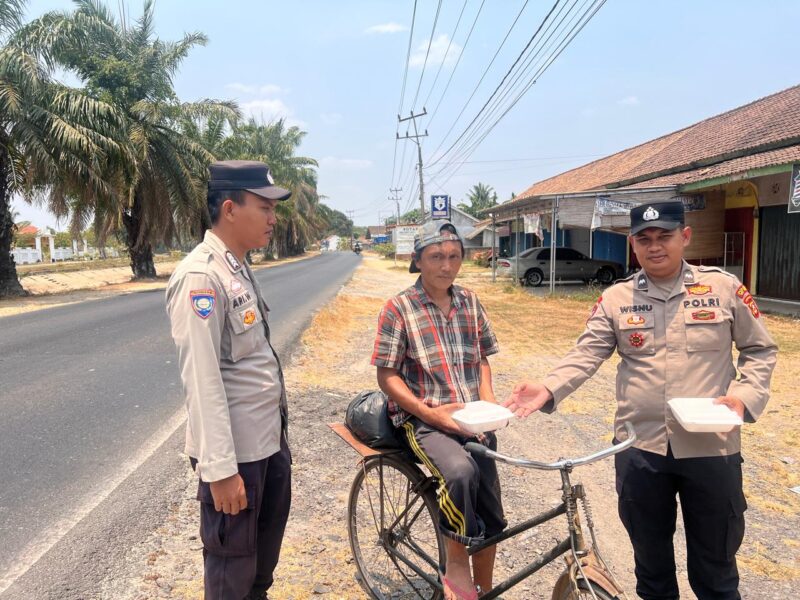 Bhabinkamtibmas Polsek Buay Madang Timur Aipda Wisnu Saputra didampingi Kanit Binmas Bripka Ari Wicaksono membagikan paket makanan kepada seorang warga pesepeda di Desa Karang Tengah, Kecamatan Buay Madang Timur, Kabupaten OKU Timur.