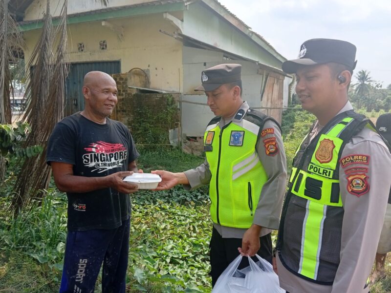 Ka SPKT Polsek Buay Madang Timur Aipda Khoirul Alkaf menyerahkan paket makanan siap saji kepada seorang warga dalam kegiatan sedekah dan berbagi di seputaran wilayah Desa Karang Tengah, Kecamatan Buay Madang Timur, Kabupaten OKU Timur.