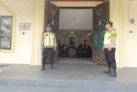 Personel Polsek Buay Madang Timur, Aipda Khoirul Alkaf dan Bripka Nur Kholik, bersiaga di depan pintu masuk Gereja Trinitas Bangun Sari BK 3, Kecamatan Buay Madang Timur, Kabupaten OKU Timur, Sumatera Selatan.