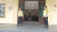 Personel Polsek Buay Madang Timur, Aipda Khoirul Alkaf dan Bripka Nur Kholik, bersiaga di depan pintu masuk Gereja Trinitas Bangun Sari BK 3, Kecamatan Buay Madang Timur, Kabupaten OKU Timur, Sumatera Selatan.