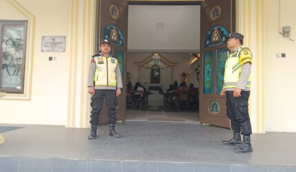 Personel Polsek Buay Madang Timur, Aipda Khoirul Alkaf dan Bripka Nur Kholik, bersiaga di depan pintu masuk Gereja Trinitas Bangun Sari BK 3, Kecamatan Buay Madang Timur, Kabupaten OKU Timur, Sumatera Selatan.