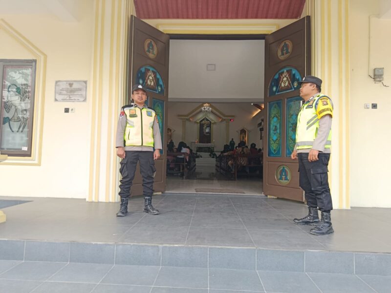 Personel Polsek Buay Madang Timur, Aipda Khoirul Alkaf dan Bripka Nur Kholik, bersiaga di depan pintu masuk Gereja Trinitas Bangun Sari BK 3, Kecamatan Buay Madang Timur, Kabupaten OKU Timur, Sumatera Selatan.