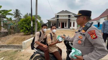 Kapolsek Buay Madang Timur Iptu Swisspo, menyerahkan paket makanan kepada sejumlah pelajar sekolah yang melintas di Desa Sumber Asri, Kecamatan Buay Madang Timur, Kabupaten OKU Timur.