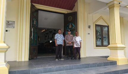 Personel Polsek Buay Madang Timur bersama pengurus gereja melakukan penjagaan di depan pintu masuk Gereja Trinitas Bangun Sari BK 3, Kecamatan Buay Madang Timur, Kabupaten OKU Timur.