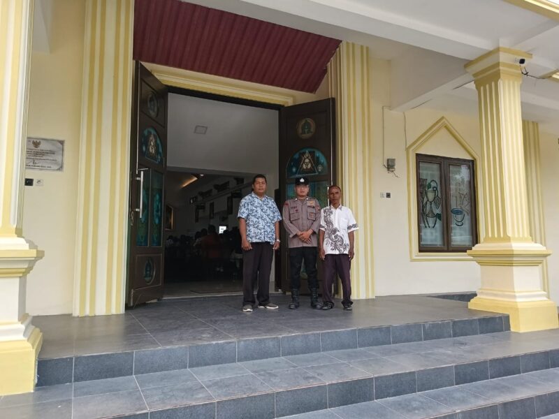 Personel Polsek Buay Madang Timur bersama pengurus gereja melakukan penjagaan di depan pintu masuk Gereja Trinitas Bangun Sari BK 3, Kecamatan Buay Madang Timur, Kabupaten OKU Timur.